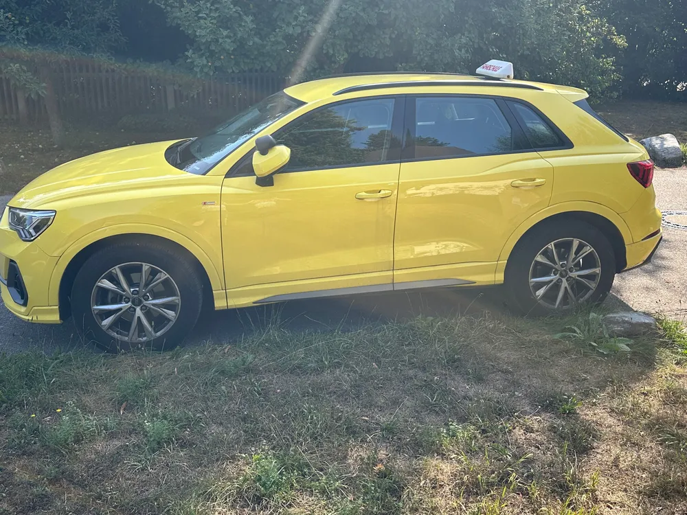 Der citrusgelbe Audi Q3 mit Fahrschul-Dachschild in der Seitenansicht